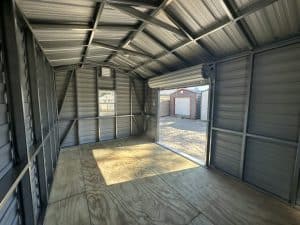 Interior view of a Robin Sheds metal storage building with a wooden floor and open door, showing outdoor storage units.