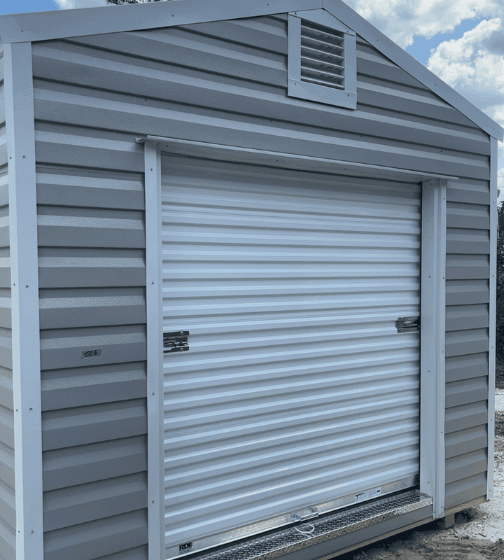 Front view of 10x20 Ash Gray Steel Americana Shed with White trim and Galvalume roof, featuring 72" roll-up coil door and two colonial windows
